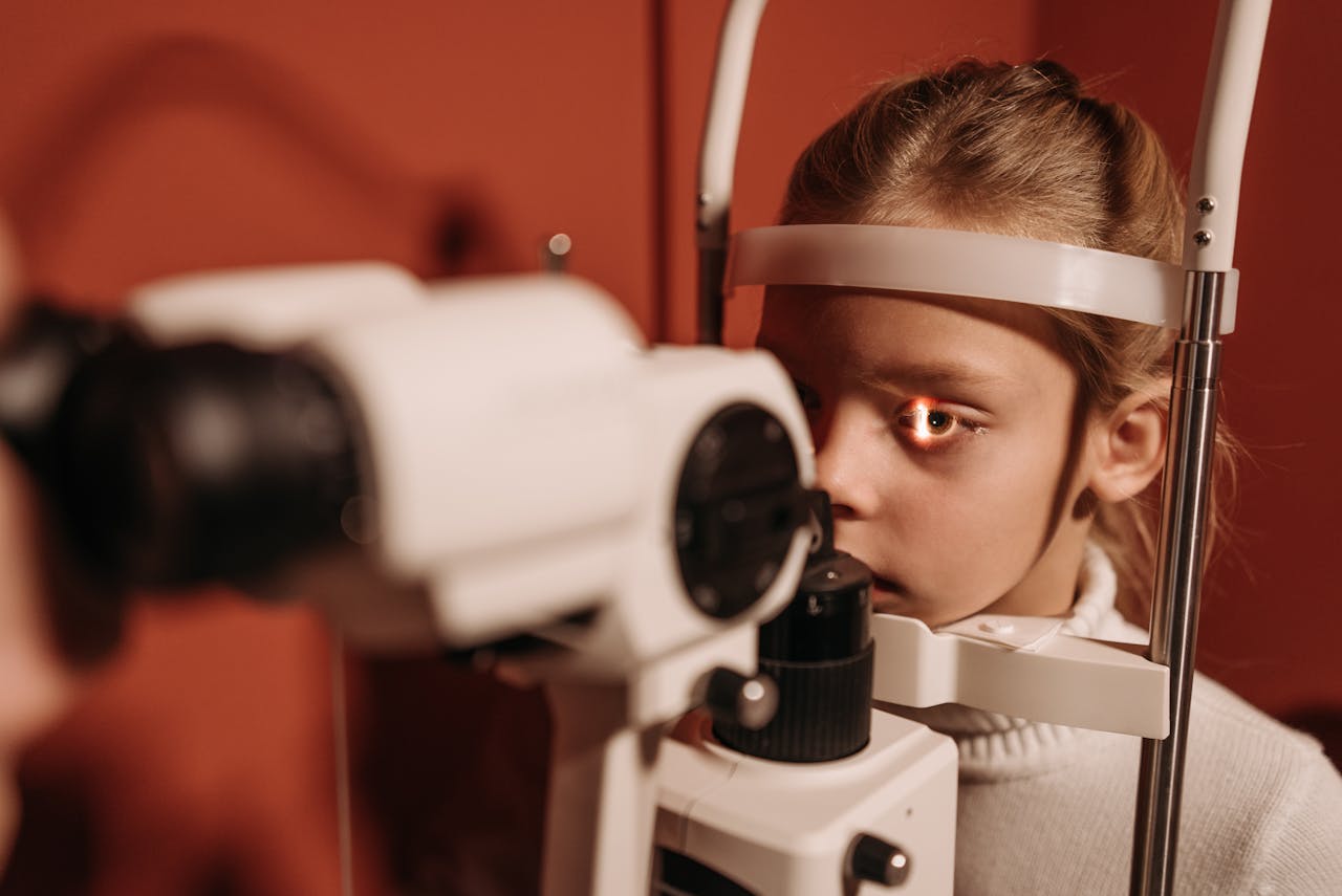 A young girl receives an eye exam using advanced optical equipment in a clinical setting.